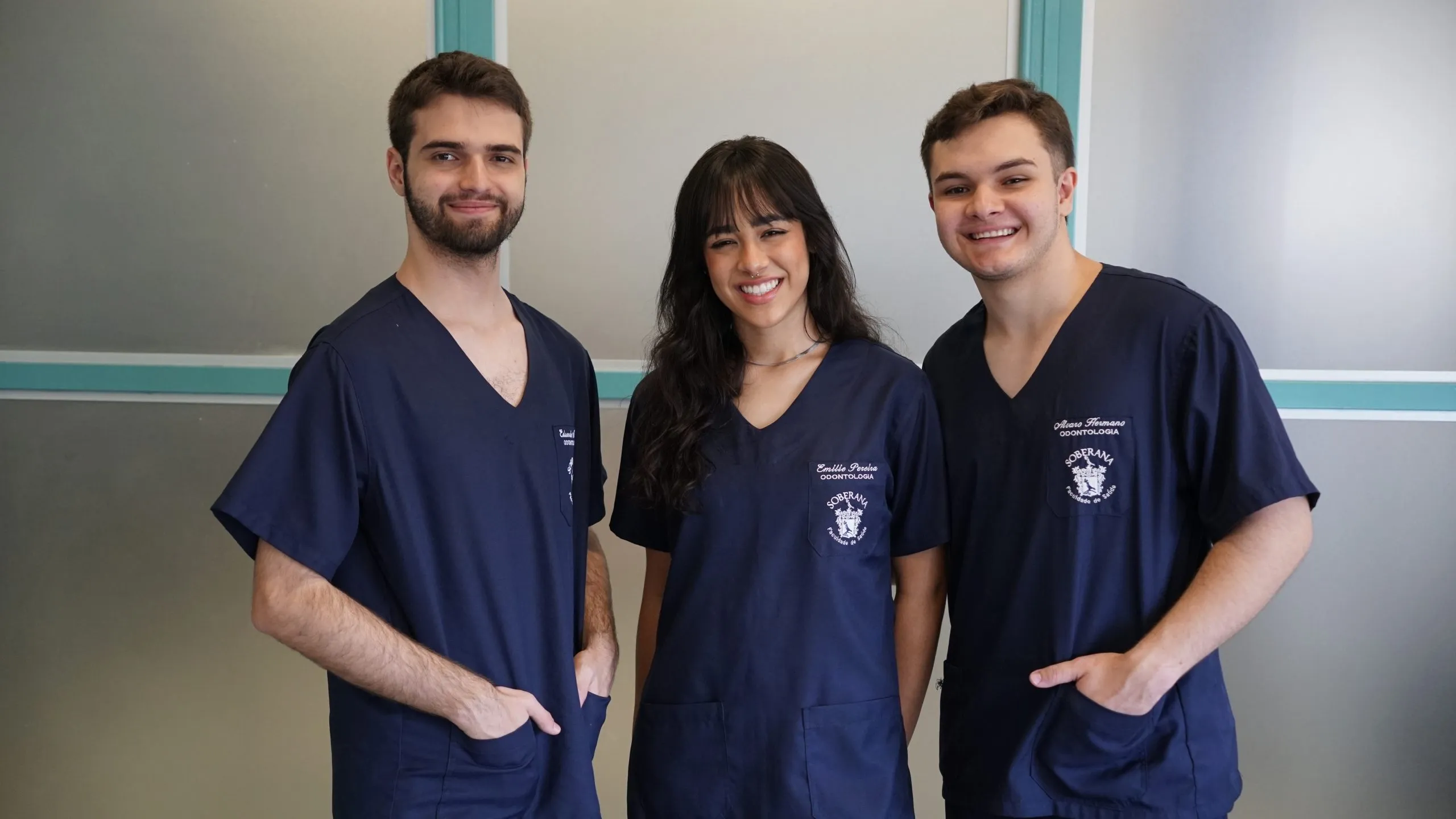 Dentistas recém-formados como alunos da soberana. nas extremidades dois rapazes e no meio uma menina. Todos trajam pijama cirúrgico na cor azul marinho