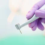 Mão trajando luva lilás segura um motor de dentista ilustrando como é possível conciliar estudo e prática na Odontologia